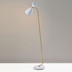 a floor lamp with a white base and a gold colored metal arm, on top of a white table