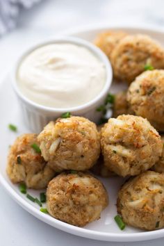 a white plate topped with crab cakes next to a small bowl of ranch dressing on the side