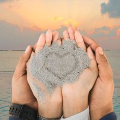 two hands are holding sand in the shape of a heart on top of each other