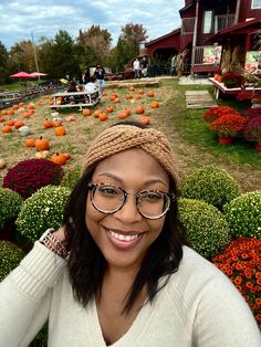 a woman wearing glasses and a knitted hat smiles in front of pumpkins on display