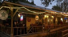 the outside of a restaurant with lights strung from it's roof and wooden railings