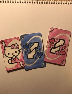 three hello kitty playing cards are shown on a notepad, one is pink and the other is blue