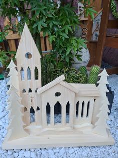 a wooden model of a church surrounded by trees and rocks in front of a potted plant