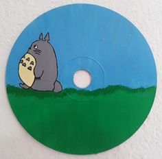 a blue and green disk with a cartoon character on the disc, in front of a white wall