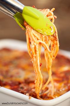 a green spatula lifting up some spaghetti from a white casserole dish