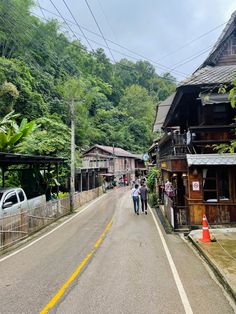 two people walking down the street in front of some houses and trees with mountains in the background