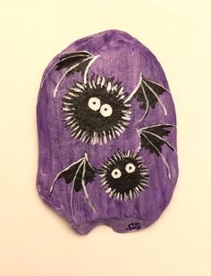 a purple piece of art with black bats on it's face and eyes, hanging from the wall