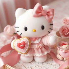 a hello kitty figurine holding a heart shaped cookie next to some pink roses