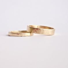 two gold wedding rings sitting next to each other on a white surface with no background