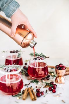 someone is pouring red wine into glasses with berries and greenery on the table next to them