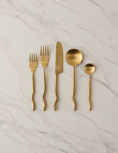 four gold forks, two spoons and one knife on a white marble countertop