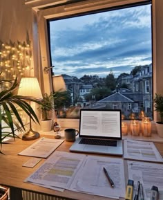 an open laptop computer sitting on top of a wooden desk in front of a window