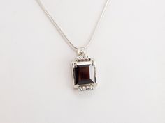 We transformed a Retro Era watch into this dazzling pendant! The garnet is exquisite, its deep scarlet hue brought to life with vibrant flashes of color from within. An array of diamond accents extends the sparkle to the entire pendant, creating a design that is truly glamorous.This pendant does not come with the chain shown. Please feel free to contact us, we will help you find the perfect chain for your style and budget!Metal: 14K White GoldGem: Pyrope Garnet totaling 6.00 CaratsGem Measurements: 13.5 x 11.6 mm, Emerald Cut Accents: 9 Diamonds totaling .36 Carats, SI1 in Clarity, H in ColorMeasurements: 27 x 14 mm, with bail Luxury Polished Garnet Jewelry, Luxury Garnet Jewelry With Polished Finish, Luxury Garnet Pendant Necklace, Elegant Garnet Jewelry With Diamond Accents, Elegant Garnet Jewelry With Gemstone Accents, Elegant Garnet Pendant Necklace, Elegant Garnet Necklace For Formal Occasions, Formal Garnet Jewelry With Gemstone Accents, Pyrope Garnet