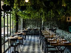 an indoor dining area with tables and chairs covered in greenery hanging from the ceiling