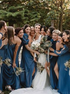 a group of women standing next to each other in front of trees and bushes wearing blue dresses