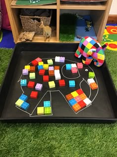 a child's play area with toy blocks on the black tray and green grass