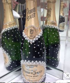 three bottles of champagne are on display in front of a glass case that is decorated with pearls