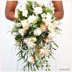 a woman holding a bouquet of white and pink flowers with greenery in her hands