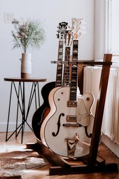 an electric guitar sitting on top of a wooden stand next to a potted plant