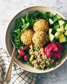 a bowl filled with vegetables and meatballs next to a fork on top of a towel