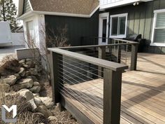 a wooden deck with metal railings next to a house in the background and rocks on the ground