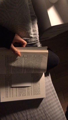 a person sitting on a bed with an open book in their lap and pointing at it