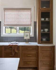 a kitchen with wooden cabinets and white counter tops, along with a beige roman blind in the window