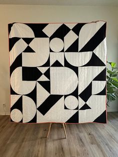 a large black and white quilt sitting on top of a wooden floor next to a potted plant