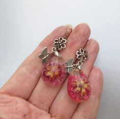 "This very pretty pair of pierced stiver-tone earrings have large oval clear plastic dangles with pink dried flowers embossed inside.  They have from pierced ear wires with have flowers plus little dangling butterflies.  They measure 2\" long and are brand new in mint condition.    FREE SHIPPING within the USA and they will arrive gift boxed!    0040" Pink Resin Flower Earrings With Pressed Flowers, Handmade Silver Resin Flower Earrings, Silver Pressed Flower Earrings In Resin, Silver Pressed Flower Resin Earrings, Silver Pressed Flower Earrings, Silver Resin Earrings With Pressed Flowers, Silver Teardrop Earrings With Pressed Flowers, Pink Dangle Earrings With Pressed Flowers, Pink Pressed Flower Drop Earrings