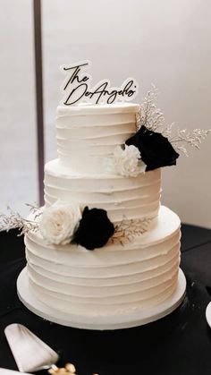 a white wedding cake with black and white flowers on the top is sitting on a table