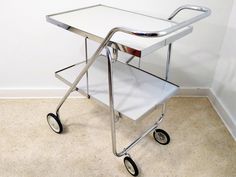 a metal and glass serving cart sitting on top of a carpeted floor next to a white wall