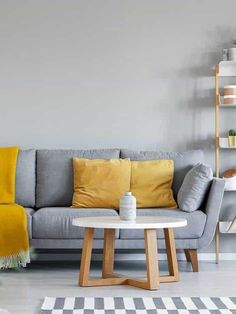 a grey couch with yellow pillows and a white coffee table in front of it on a checkered rug