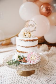 a white and gold wedding cake with pink flowers on the top is surrounded by balloons