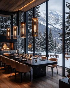 a dining room with large windows overlooking the mountains and snow covered trees is lit by pendant lights