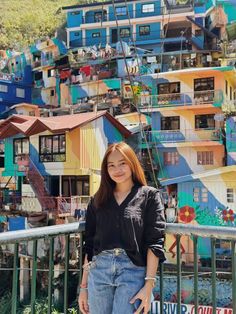 a woman standing on top of a metal railing next to colorful buildings in the background