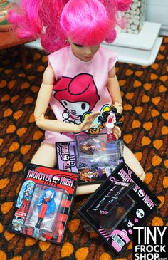 a doll with pink hair sitting on the floor next to other dolls and toys in front of her