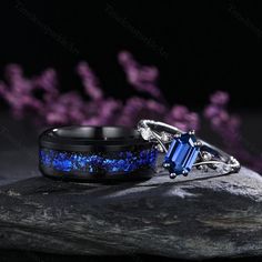 two rings with blue and white stones on them sitting on top of a rock next to purple flowers