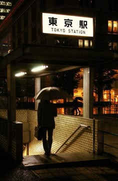 a person with an umbrella is walking down the street at night in tokyo station, japan