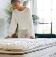 a woman in white shirt standing next to a mattress