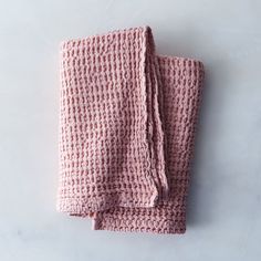 a pink knitted blanket folded on top of a white surface with the end rolled up