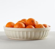 a white bowl filled with oranges on top of a table