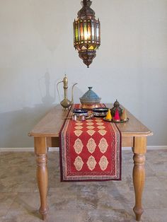 a wooden table topped with a red and gold runner next to a light hanging from the ceiling