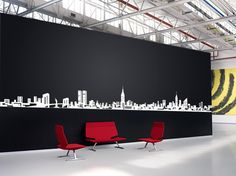 two red chairs sitting in front of a black wall with a city skyline on it