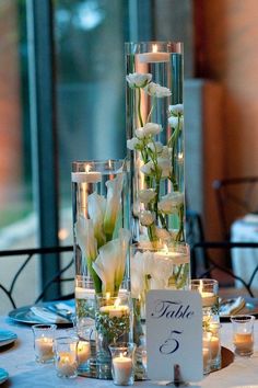 two tall vases filled with flowers and candles on top of a dining room table