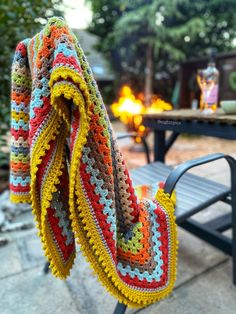 a crocheted blanket sitting on top of a bench next to a fire pit