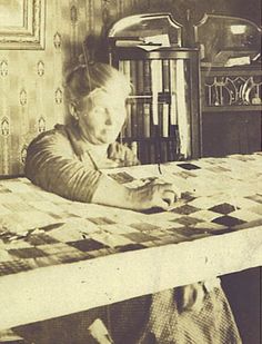 an old photo of a woman sitting at a table writing on a piece of paper