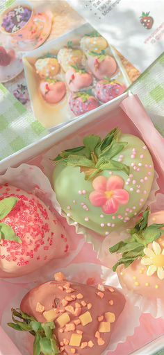 there are three decorated doughnuts in the box on the table and one is green with pink sprinkles