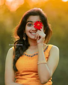 a woman holding a red flower in her hand and smiling at the camera with an orange background