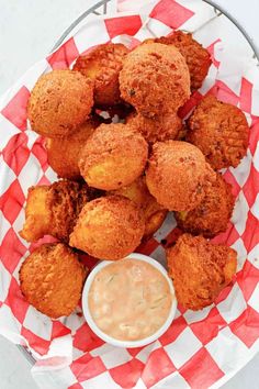 some fried food is on a red and white checkered paper with a small bowl of dipping sauce