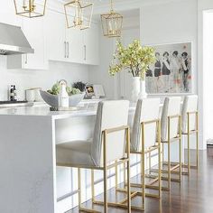 a kitchen with white counter tops and gold barstools in front of an island